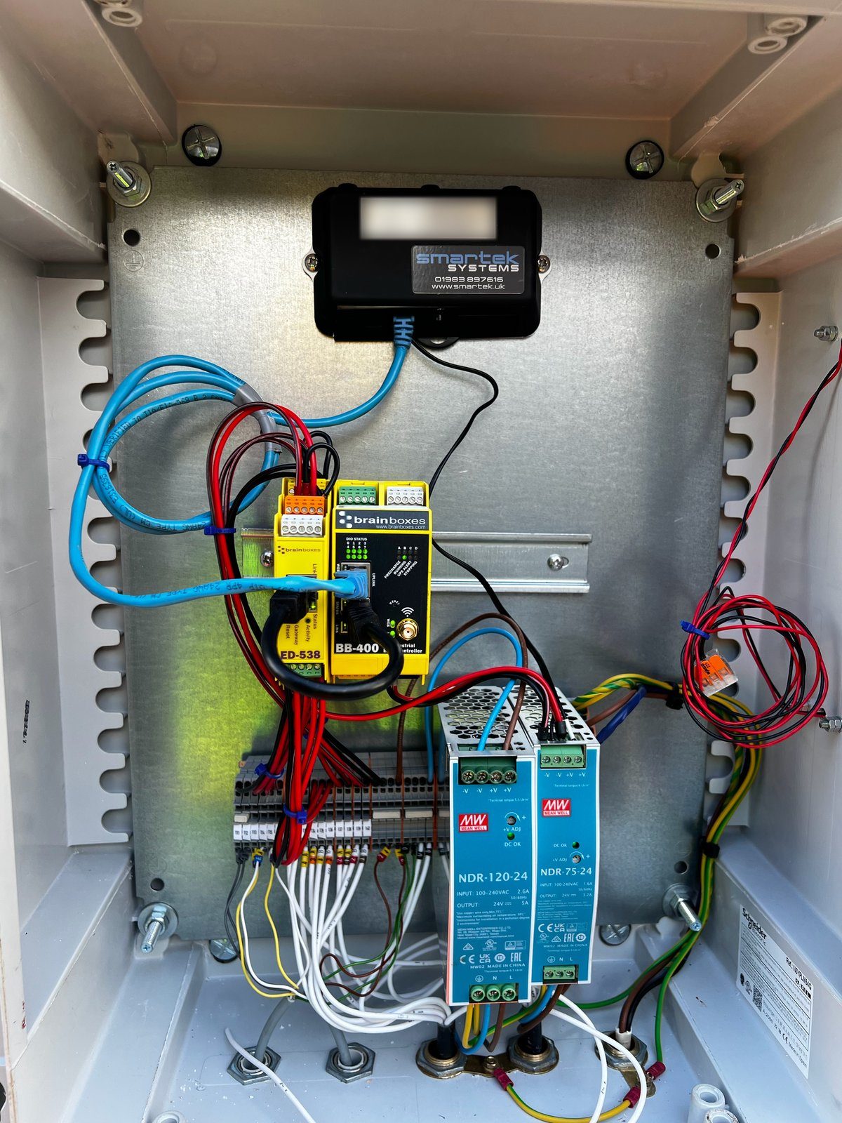 Open enclosure with a Smartek-labelled gateway, DIN-rail I/O modules, power supplies and neatly loomed wiring